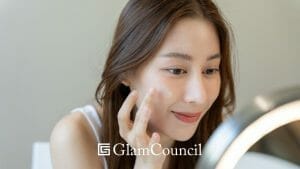 Asian woman applying facial moisturizer while looking at the mirror