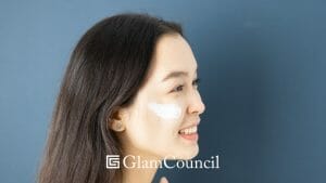 Asian woman applying facial moisturizer while smiling